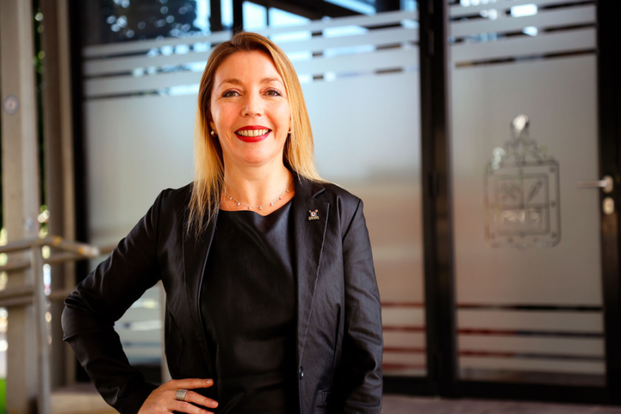 Dra. Andrea Mahn, académica de la Facultad de Ingeniería y líder del proyecto. Aparece vestida con un traje negro. De fondo, las puertas de entradas a la Facultad de Ingeniería