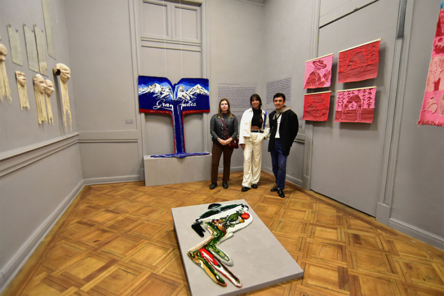 Las y el artista de Sofía Pucher, Daniela Jiménez y José Pérez, posan frente a la exposición. De fondo, una obra que juega una caja grande de fósforos correspondiente a la empresa Gran Andes, en donde la cordillera se observa esplendorosa y en el medio de ella cae el agua de los deshielos sobre su propia base.