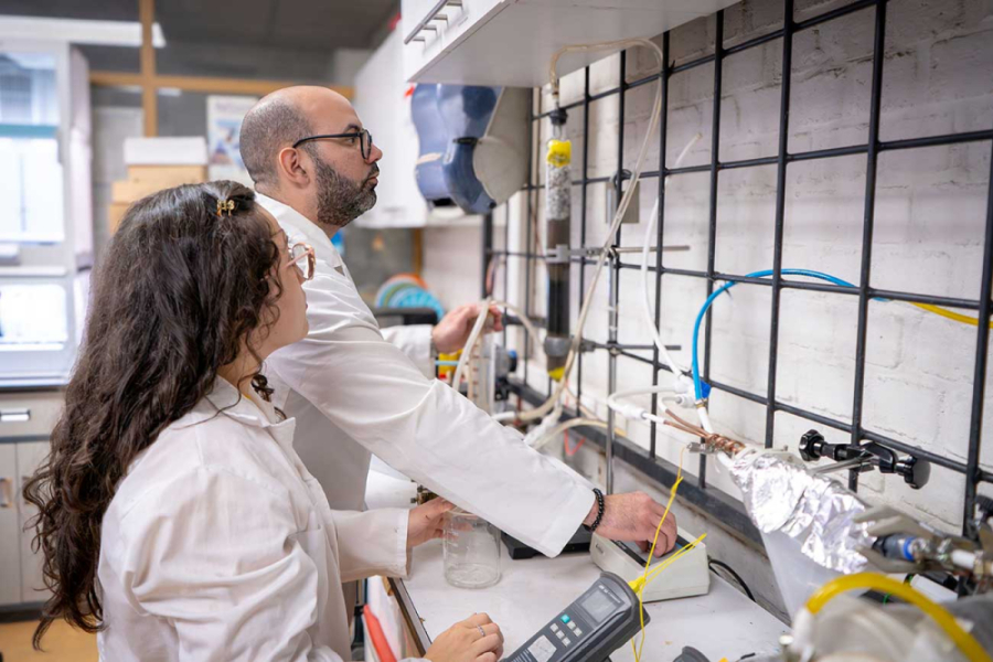 Investigadores Usach trabajan en el laboratorio. Visten delantales blancos. Una es una mujer de cabellos rizados y el hombre es calvo.