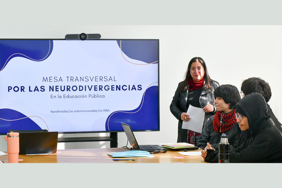 Sala de clases con profesora y tres estudiantes. Al fondo, una lámina con el nombre de la actividad