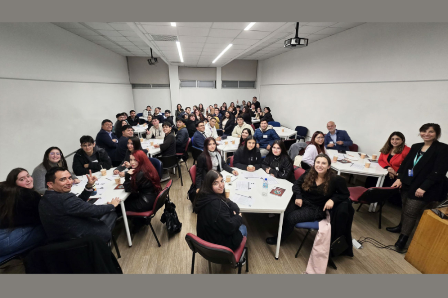 En la fotografía aparecen tutores y estudiantes que participaron de la jornada, distribuidos en diversas mesas. El fondo es una muralla blanca de la sala de reuniones en donde se realizó la actividad.