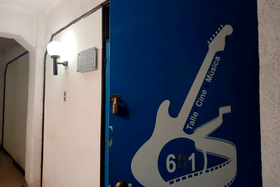 Puerta de entrada al Taller de Cine y Música VRAE -USAChH, lugar donde se realizó la muestra. De fondo se percibe una puerta azul con una guitarra eléctrica en trazos de color blanco.
