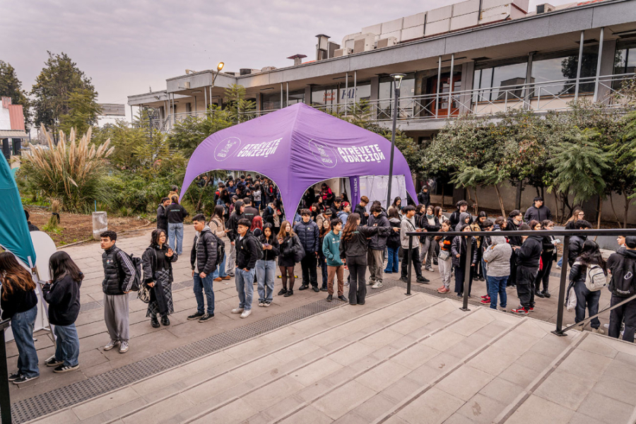 En l fotografía aparece una fila de estudiantes en las afueras del edificio nuevo de la Facultad de Administración y Economía para ingresar a desarrollar la prueba. En la imagen, también aparece un toldo morado con la frase fuerza "Atrévete Admisión"