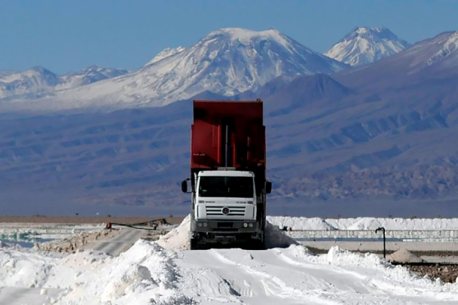 Camión minero se movilizada por carretera de litio en un salar. De fondo, la cordillera de los andes en su esplendor y el cielo celeste.