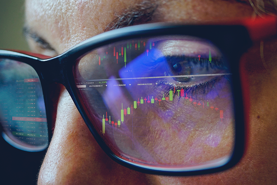 Picture of a woman wearing glasses looks at a financial chart, which is reflected in the lenses.