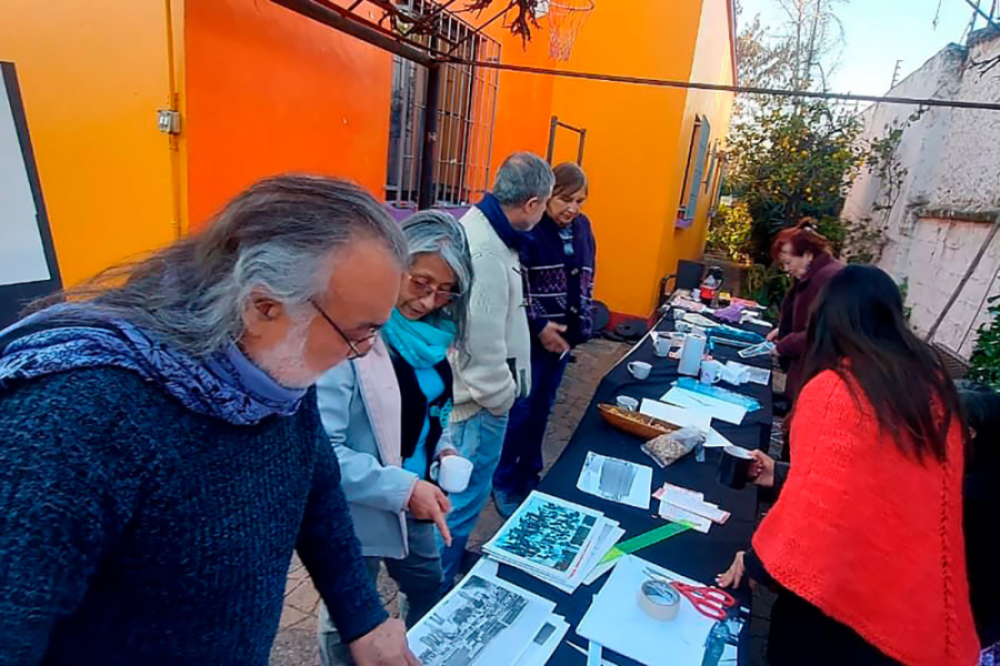 Ex estudiantes UTE-USACH revisan el material fotográfico en mesas puestas en un patio interior de una casa antigua.