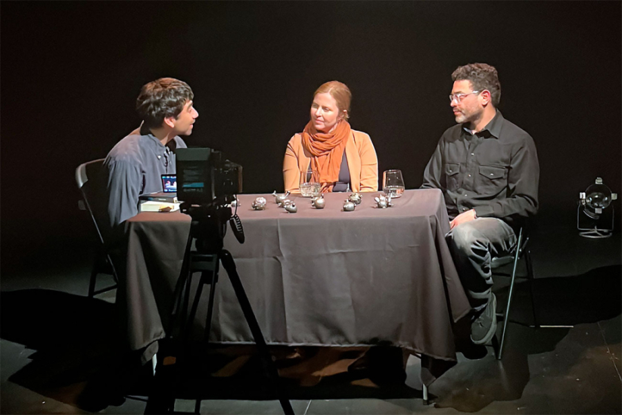 Tres personas aparecen en un set con fondo negro grabando el podscat