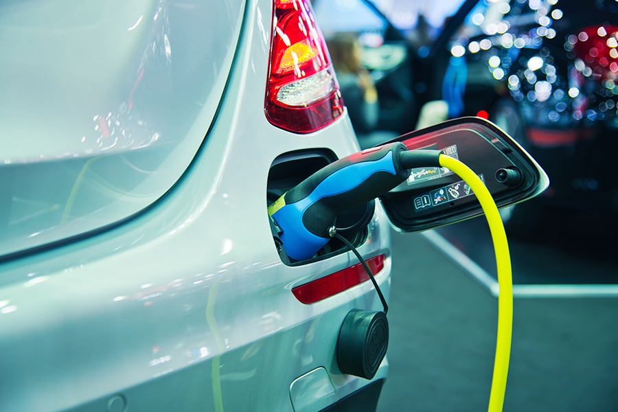 Close-up da parte traseira de um veículo elétrico prateado que está sendo conectado e carregado.