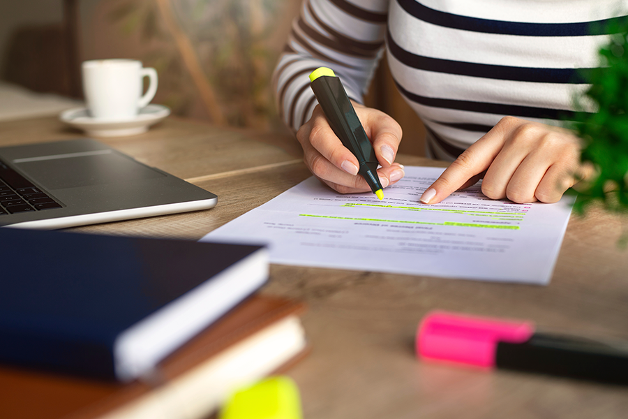 Uma pessoa com uma camisa listrada se inclina sobre uma mesa para destacar texto em um documento com um marcador amarelo fluorescente.