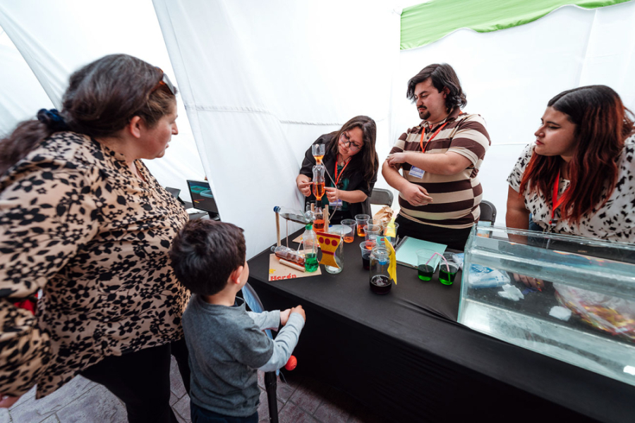 En la imagen aparece un stand de una Feria de la Ciencia anterior, en el que estudiantes y académicos enseñan sus experimentos a niños y sus familias