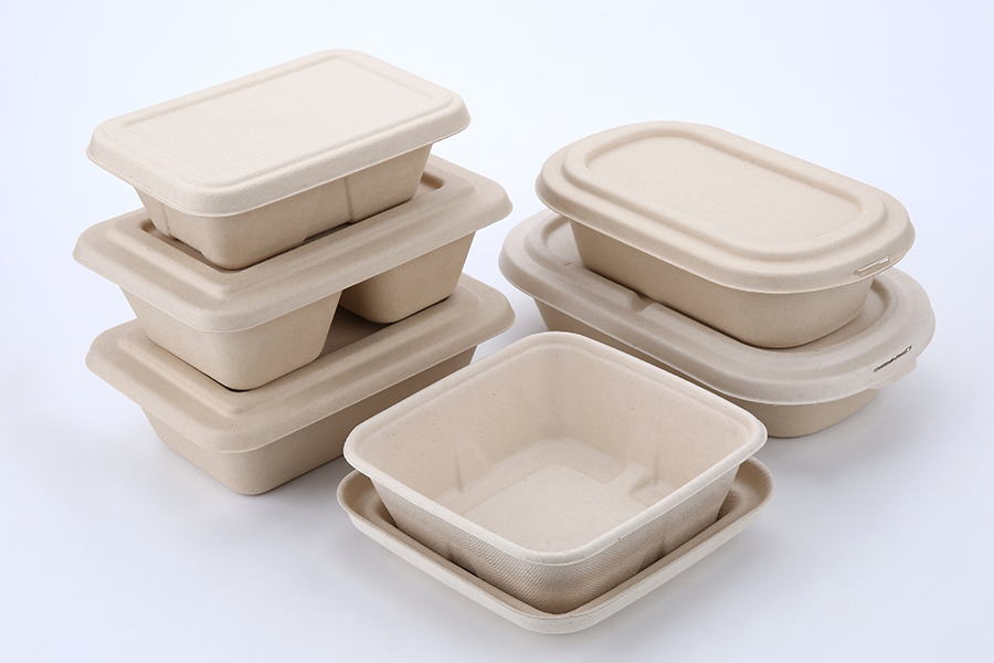 Imagem de várias pilhas de embalagens biodegradáveis para alimentos, de cor bege, retangulares e quadradas, dispostas sobre um fundo branco e limpo. 