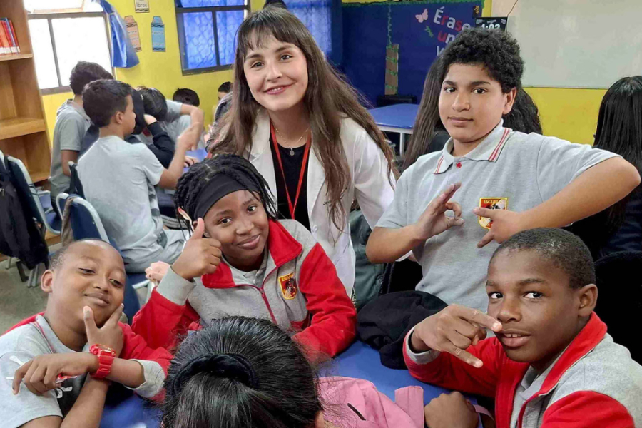 En la fotografía aparecen estudiantes de educación básica junto a una profesora en la sala de clases. Todos miran a la cámara de frente.