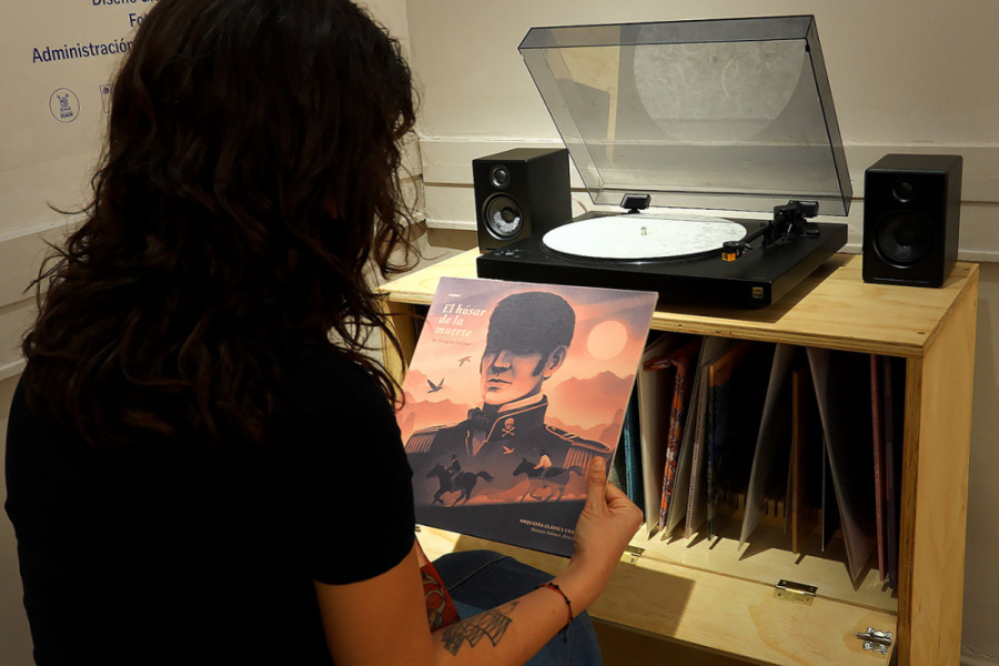 En la imagen aparece una mujer de espaldas sosteniendo el disco El Húsar de la Muerte frente a un tocadiscos.