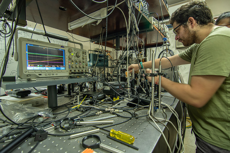 En la imagen aparece un investigador Usach y trabajando en su laboratorio que presenta máquinas, pantallas y y cables. 