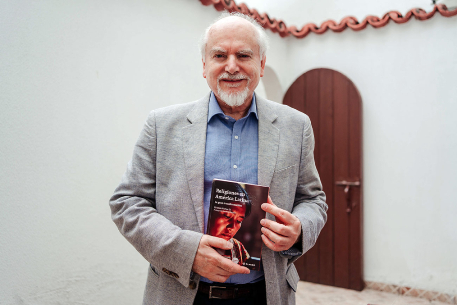En la imagen aparece el Dr. Cristián Parker, quien lleva en sus manos su nuevo libro. De fondo, un patio del Instituto de estudios avanzados Usach 