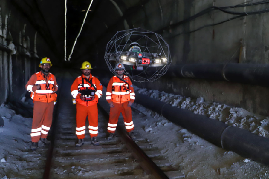 En la imagen se muestra un dron operado por tres mineros con overoles naranjos en faena bajo tierra