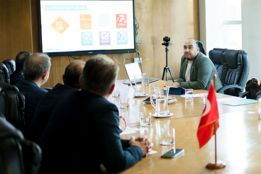 En la imagen aparece profesional del Departamento de Relaciones Internacionales e Interuniversitarias (DRII) , junto a visitas del extranjero en una reunión. En el centro hay una mesa  y de fondo se observa un power point con información