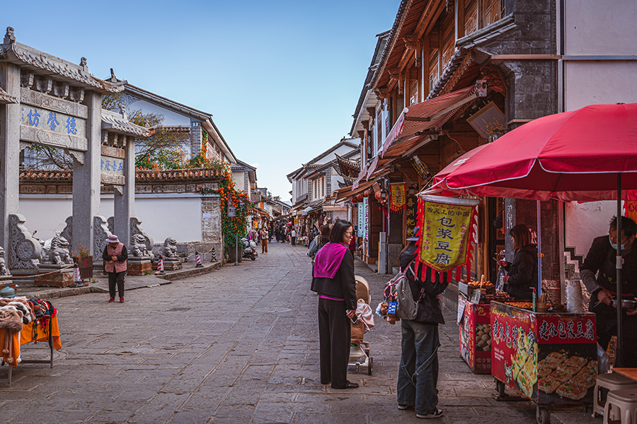 A bustling traditional street with stone paving, historic architecture, and colorful red market stalls.