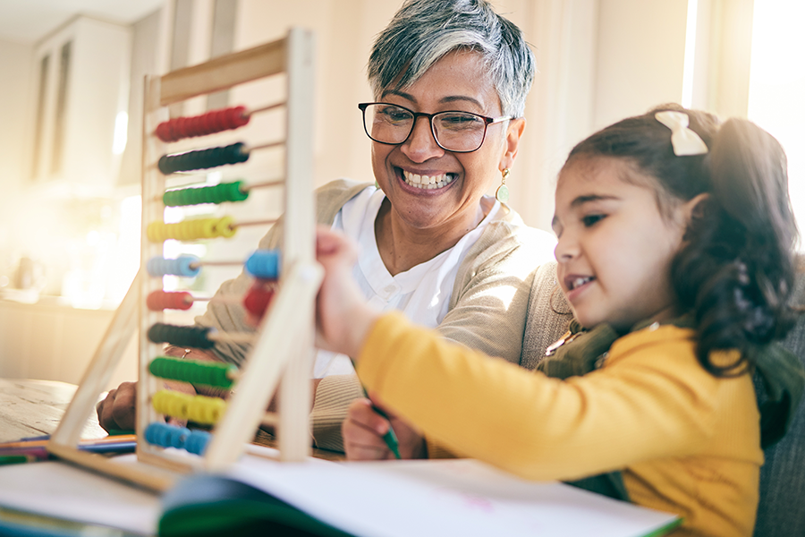 Una mujer sonriente ayuda a una niña a utilizar un colorido ábaco de madera para aprender en una mesa.