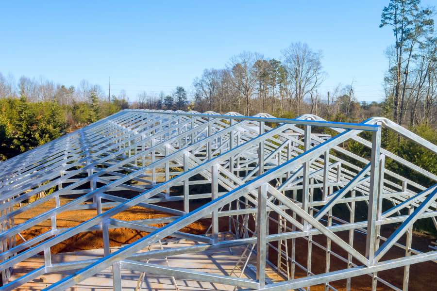 Primer plano de una gran estructura de techo metálica plateada en construcción contra un cielo azul claro.