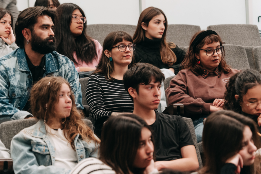 En la fotografía aparecen estudiantes asistentes al evento sentados en el auditorio