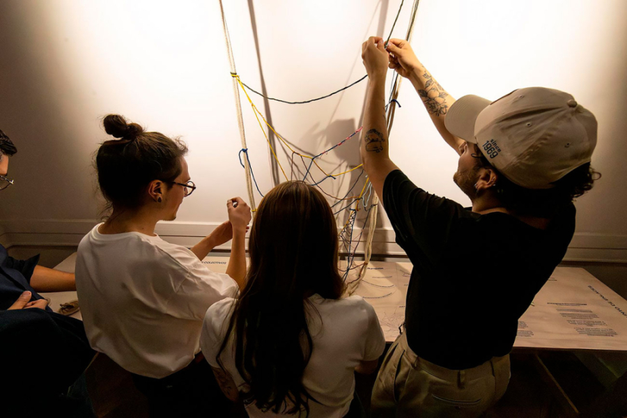 La imagen muestra a dos mujeres y un hombre explorando una de las obras textiles de la exposición
