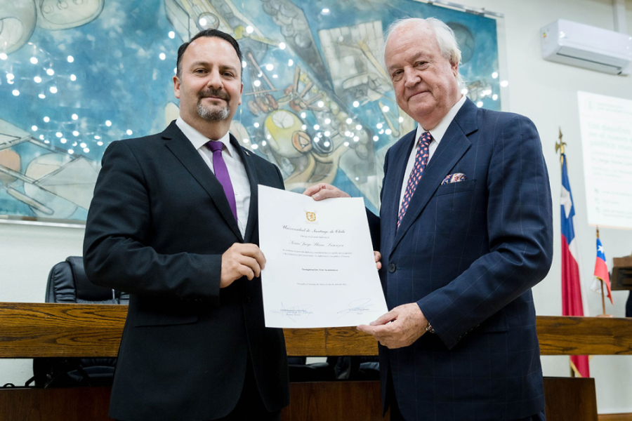 En la imagen aparece el rector (s) Usach, Dr. Juan Escrig y el ex embajador Jorge Heine. En la imagen posan junto con un testimonio por su presentación en el inicio del año académico 2026 en el Salón de Honor Usach. De Fondo, el cuadro del pintor Roberto Matta.