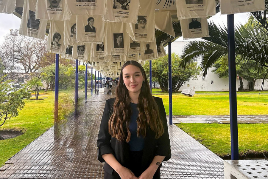 La imagen muestra a la egresada posando frente a la cámara, en uno de los pasillos de la universidad