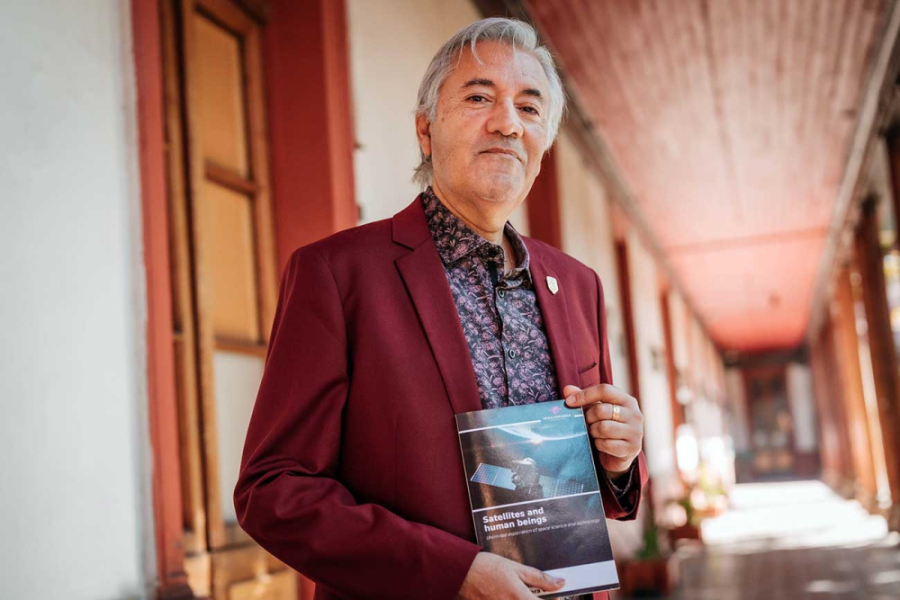 La imagen muestra al profesor con el libro en sus manos en un pasillo del edificio EAO