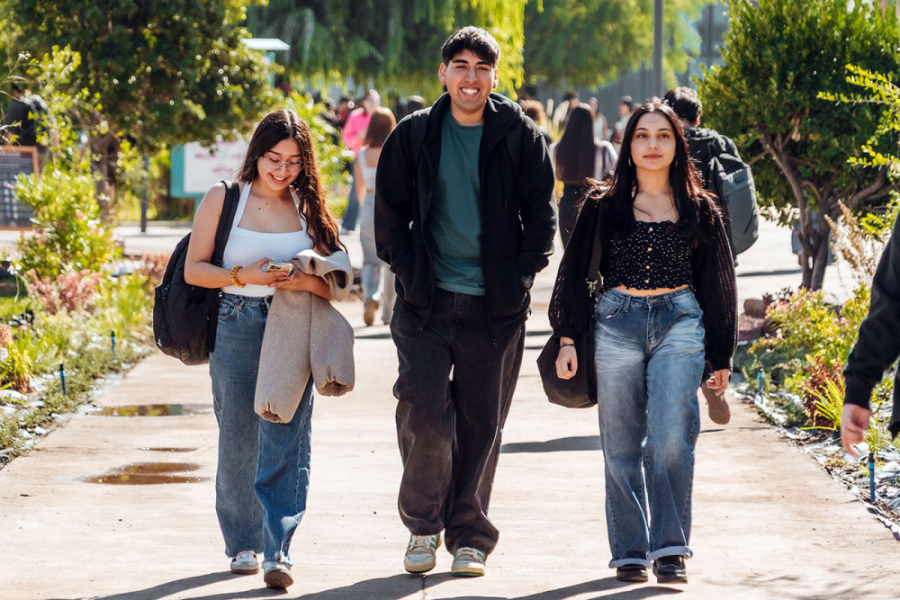 En la fotografía aparecen tres estudiantes del a Usach, dos mujeres y en medio un hombre, que camina alegres por el Campus Central.