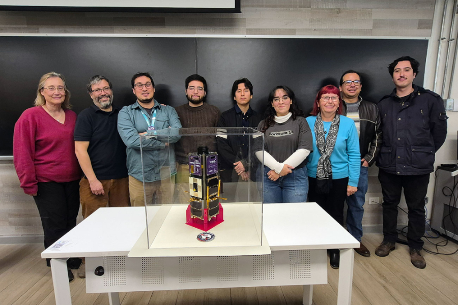 La imagen muestra a las y los participantes del proyecto posando frente al nanosatélite 