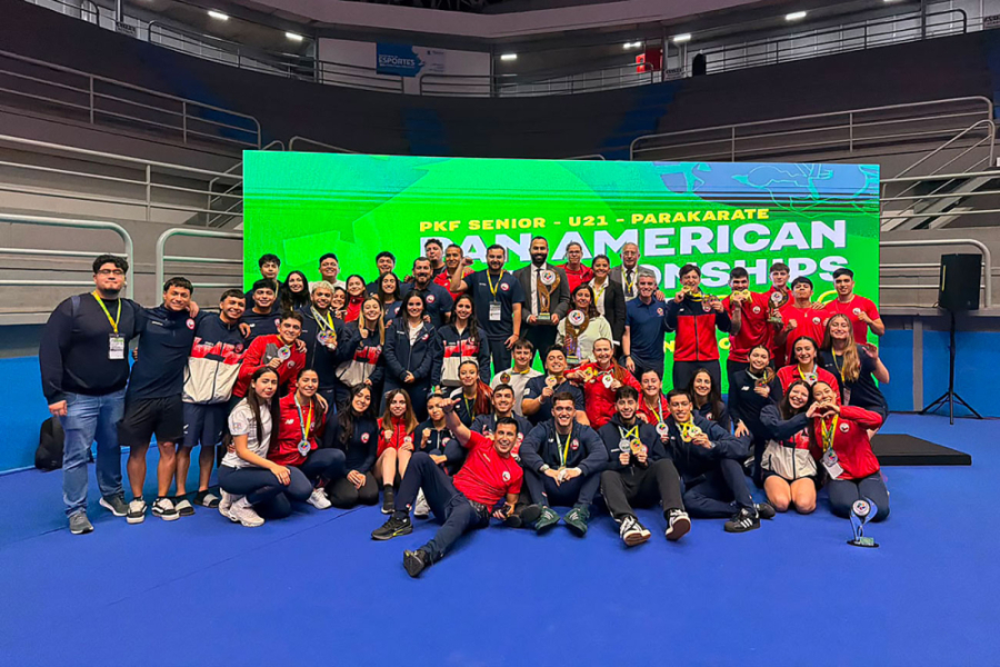 La imagen muestra al equipo completo de la selección chilena de karate posando con sus premios en el escenario principal del evento