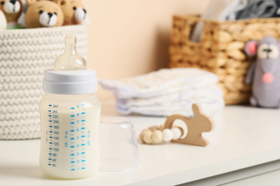 A close-up of a bottle of milk, surrounded by diapers and toys.