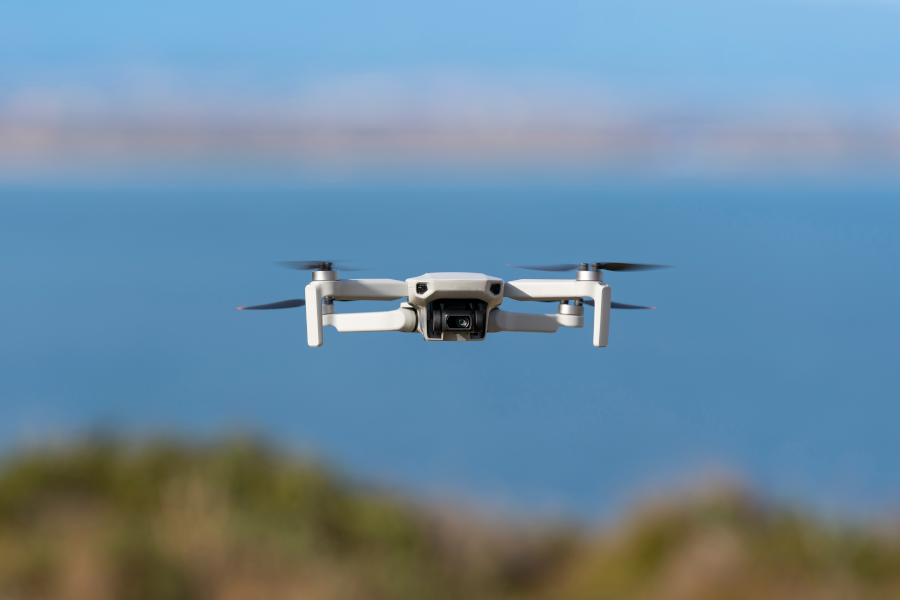 White drone hovering in the air over a blue ocean.