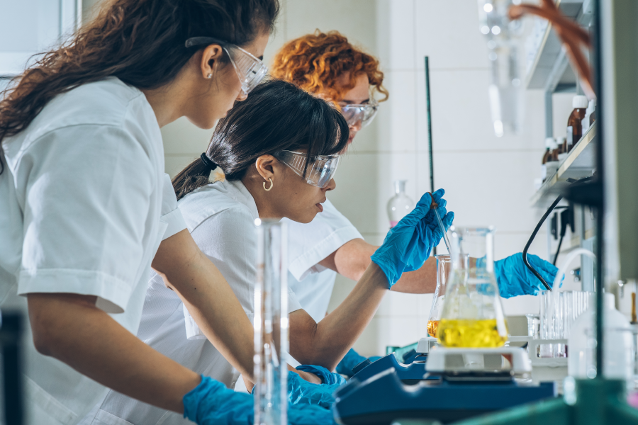Tres científicas con gafas y guantes trabajan en un laboratorio.