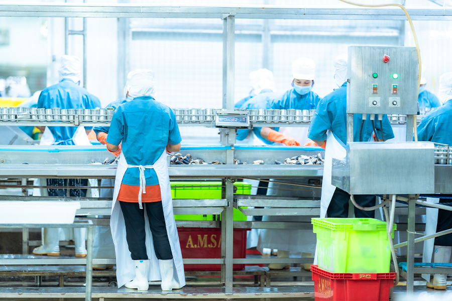 Factory workers in protective gear processing food on assembly line. 