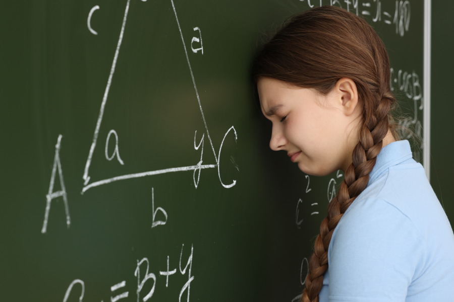 A frustrated-looking girl resting her forehead against a blackboard with a geometry problem on it.