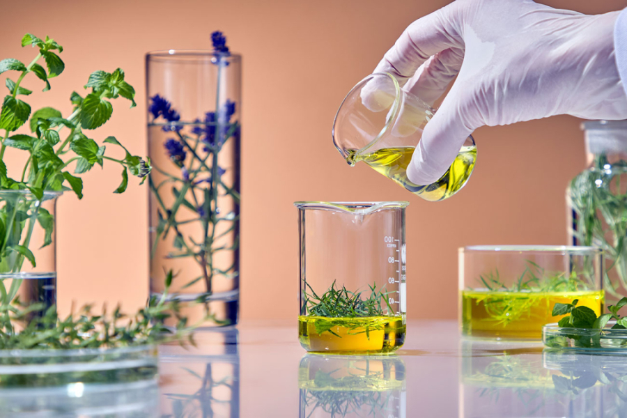 En la imagen aparece una mano enguantada de científico trabajando con recipientes plantas y aceites.