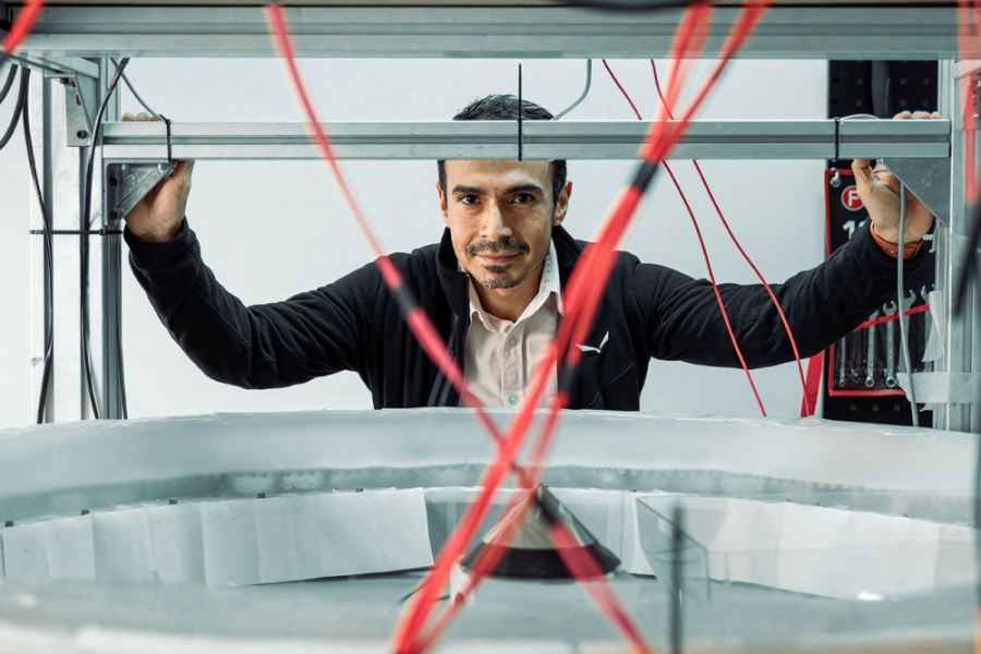 La foto muestra al académico en su laboratorio, detrás de una máquina y cables rojos