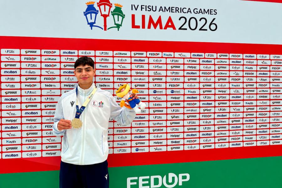 En la fotografía aparece Víctor Jara, estudiante Usach quien logró una destacada actuación en FISU America Games 2026.. Aparece con una chaqueta de buzo blanca, una de sus medallas y la mascota del evento. De fondo, un panel con los sponsor del evento.